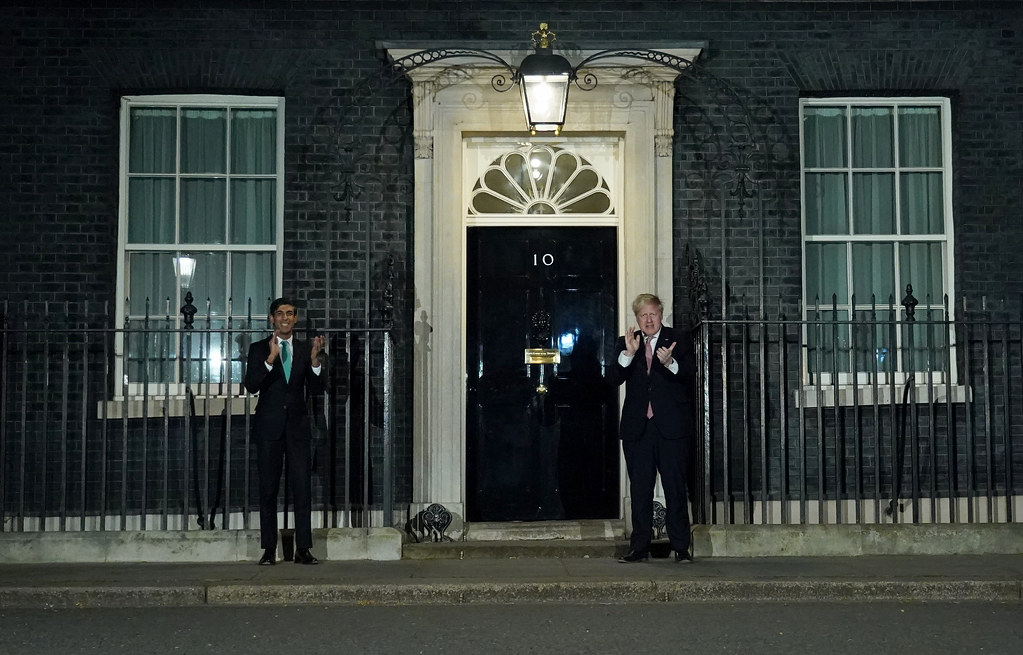 "Boris Johnson and Rishi Sunak 'Clap for our Carers'" by UK Prime Minister is licensed under CC BY-NC-ND 2.0. UK Coup